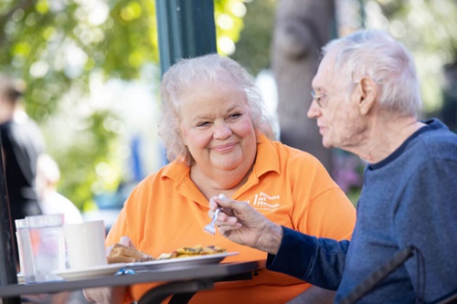Female right at home caregiver watching senior male client eat at a cafe outside